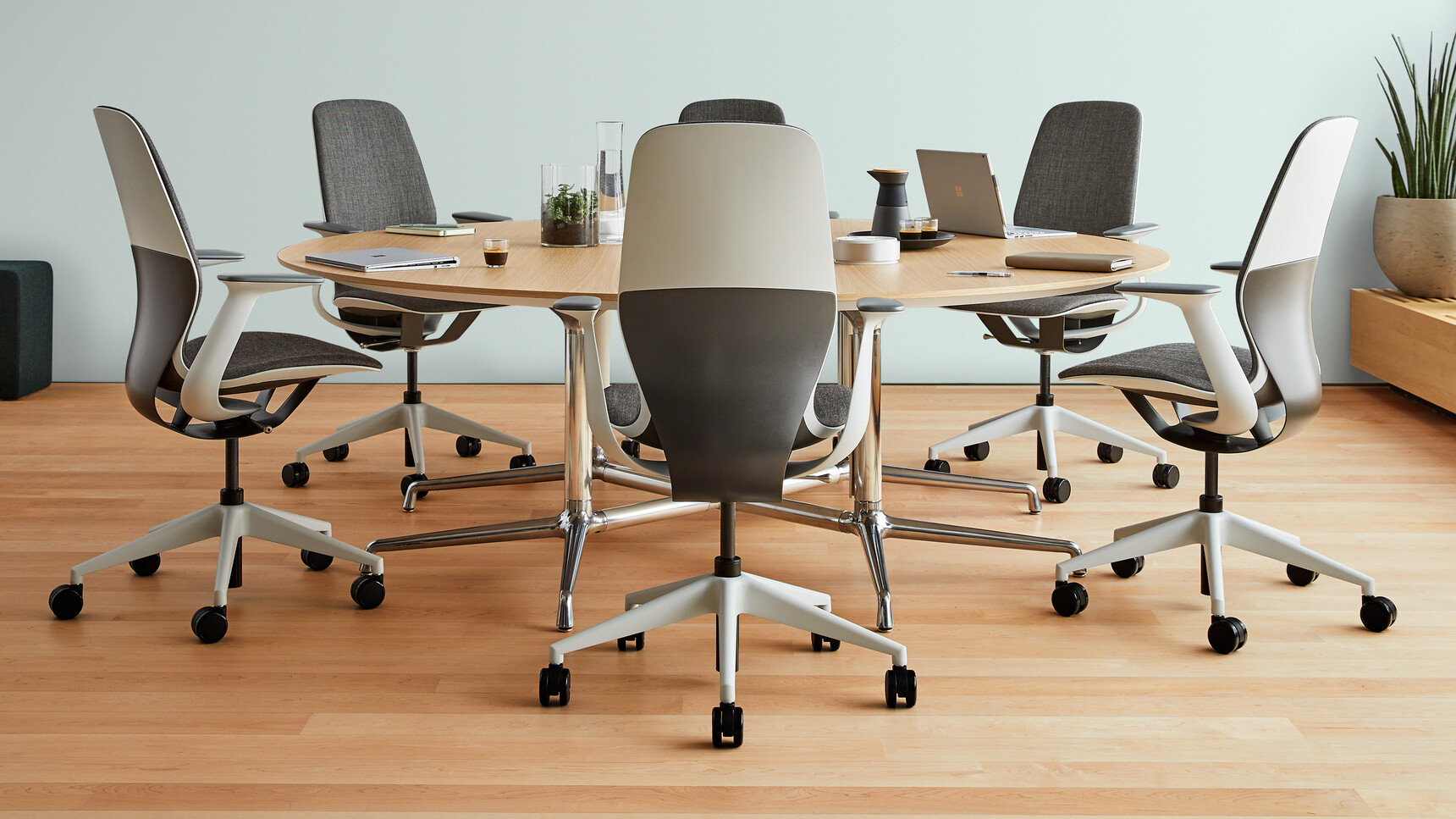 Six Steelcase SilQ Upholstered Office Chairs With Grey Upholstery With Light Grey Legs On Castors And Light Grey Fixed Arms And Black Light Grey Frame At Fixed Meeting Table With Wood Finish In Meeting Room