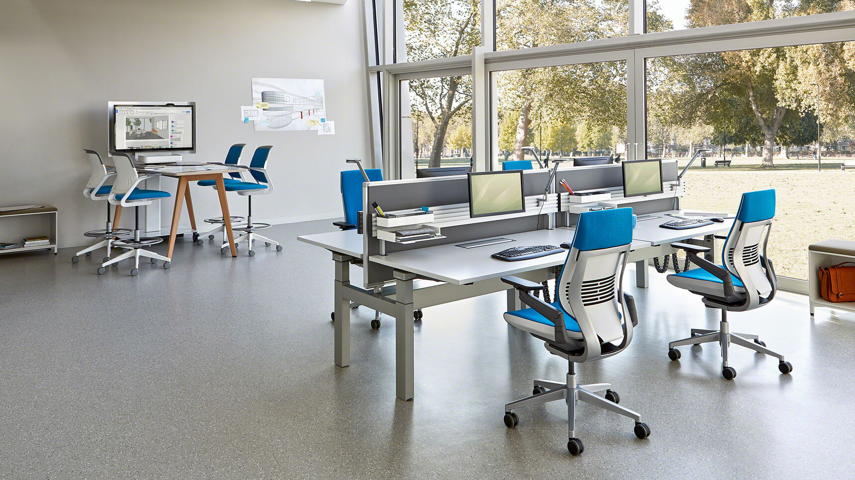 Four Steelcase Gesture Wrapped Back Office Chairs In Blue Upholstery With White Grey Frame And Black Armrests And Grey Base Finish On Castors At Height Adjustable Bench Desks With White Table Top And Grey Leg Finish