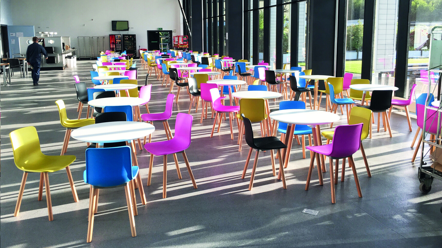 A Group Of Elite Ben Chairs In Black Blue Pink And Yellow At Desks In A Canteen