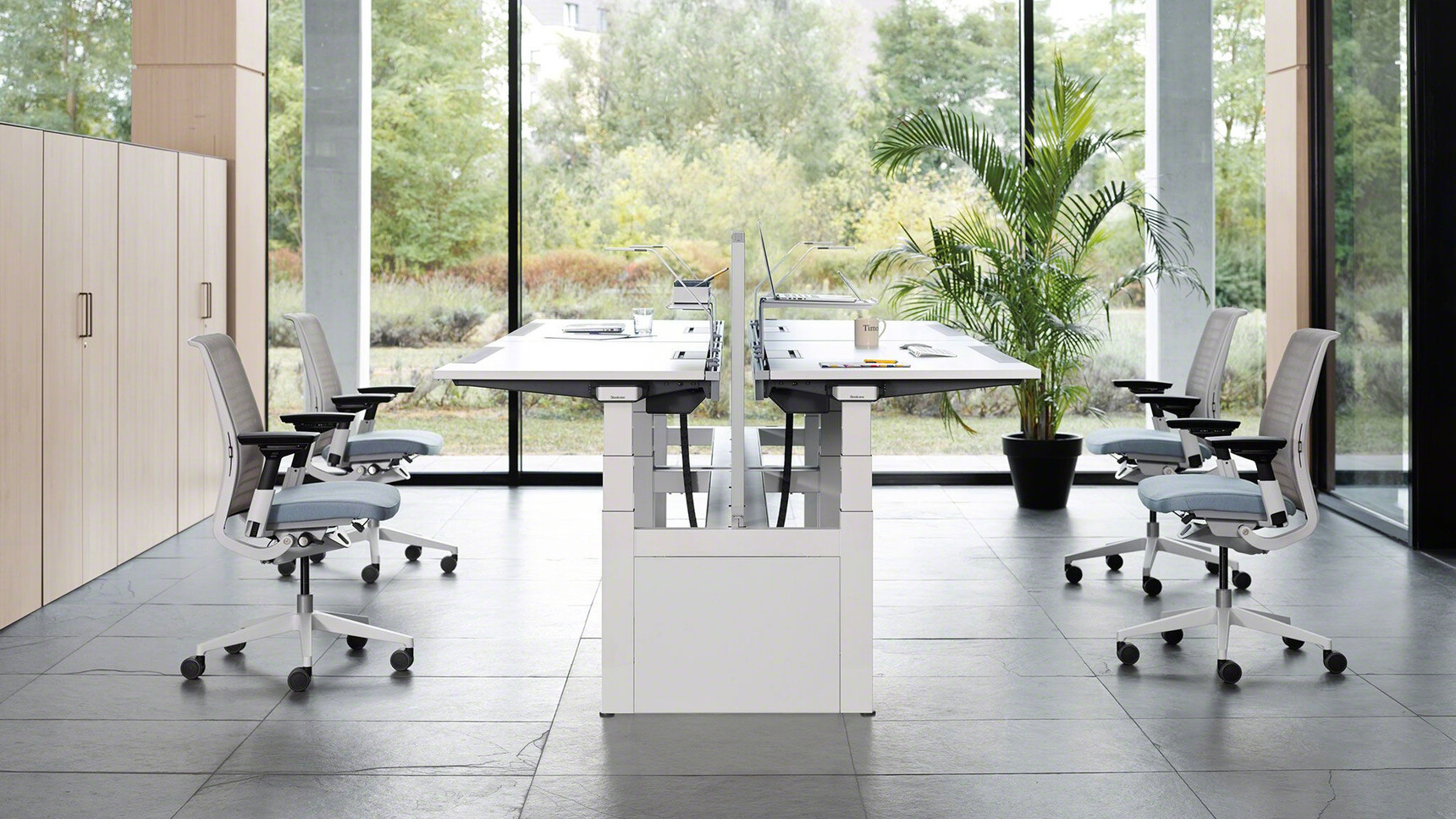 Two Steelcase Ology Height Adjustable Bench Desks With White Finish And Four Think 3D Knit Office Chairs With Blue Upholstery At Desks