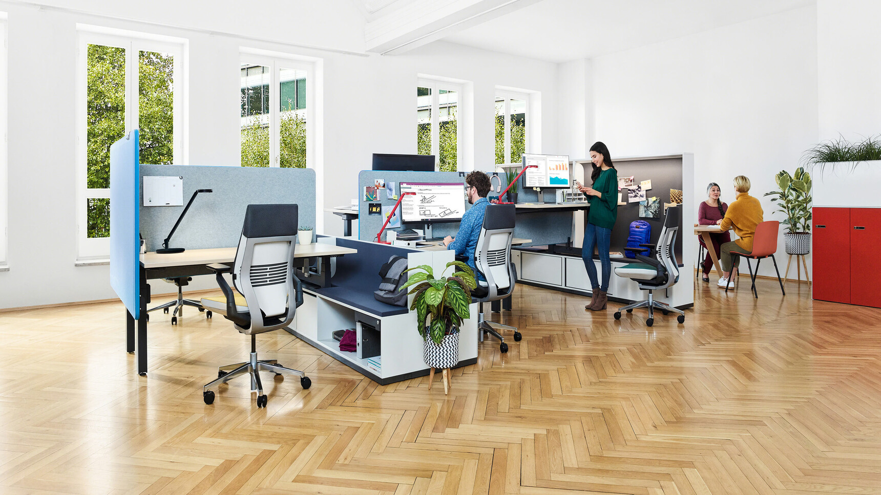 Three Steelcase Ology Height Adjustable Bench Desks With Simple Touch With Wood Table Tops And Black Legs With Four Gesture Wrapped Back Office Chairs With Blue Upholstery