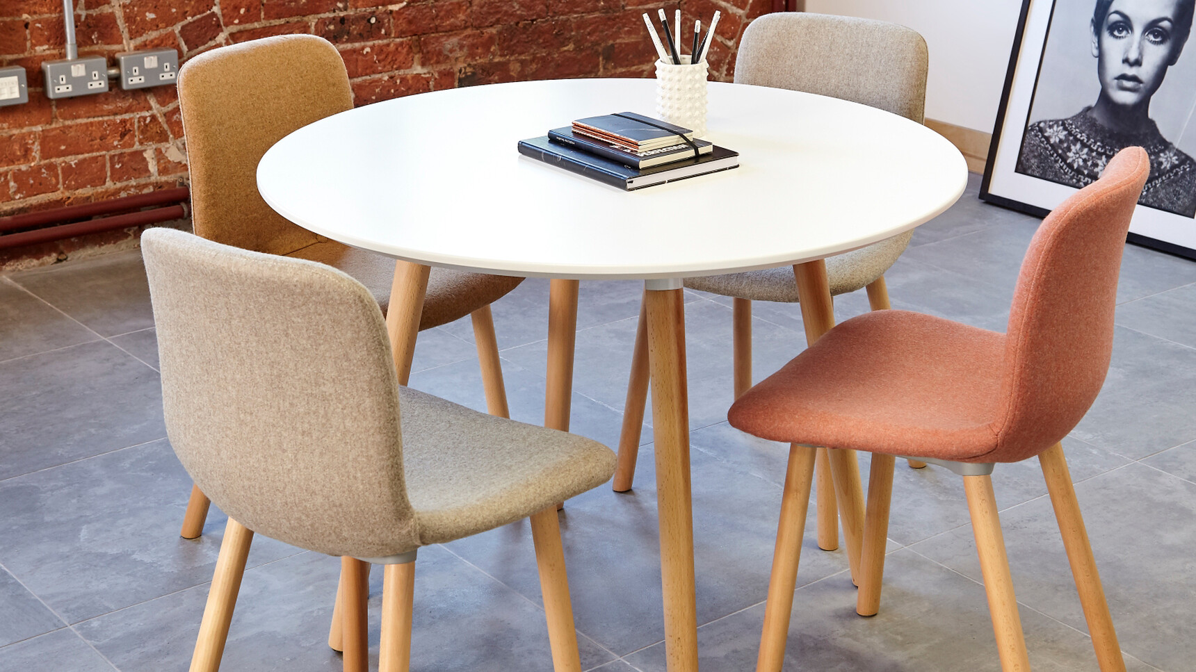Elite Tondo Circular Meeting Table With White Table Top Finish With Wood Leg Finish With Four Ben Upholstered Chairs Two In Grey One Brown And One Orange Upholstery At Desk