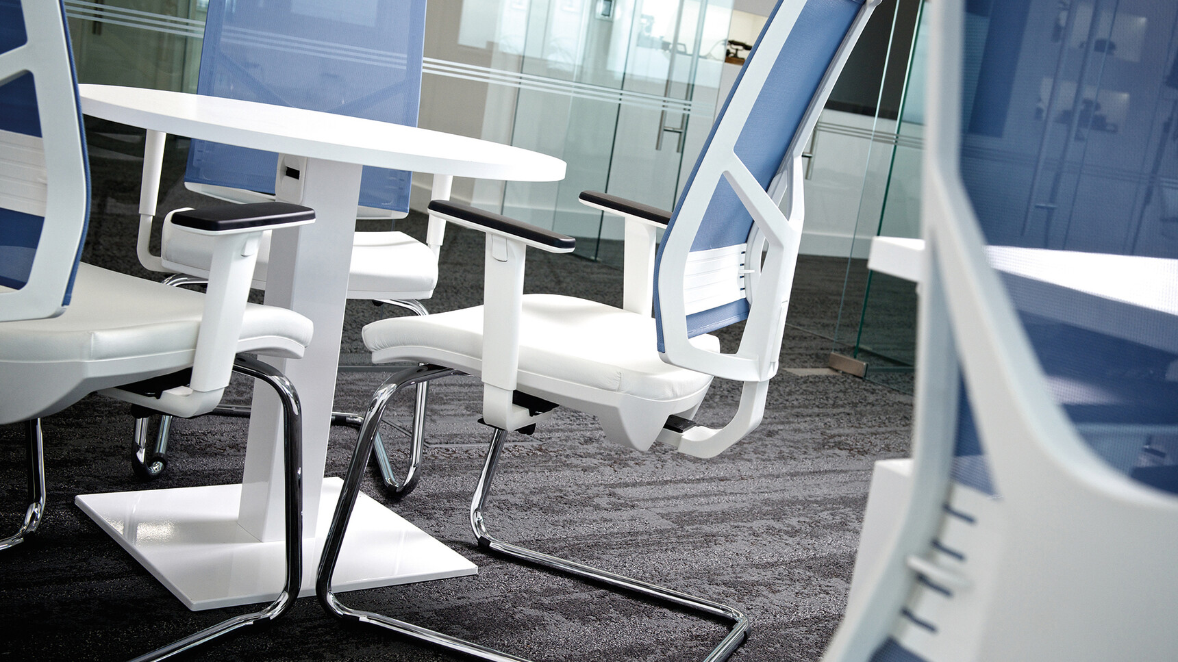 Elite Circular Meeting Table with Wire Managed Base With A White Finish With Four Vida Mesh Back Cantilever Meeting Chairs In White Upholstery And Blue Backrest And Chrome Legs In Office Environment