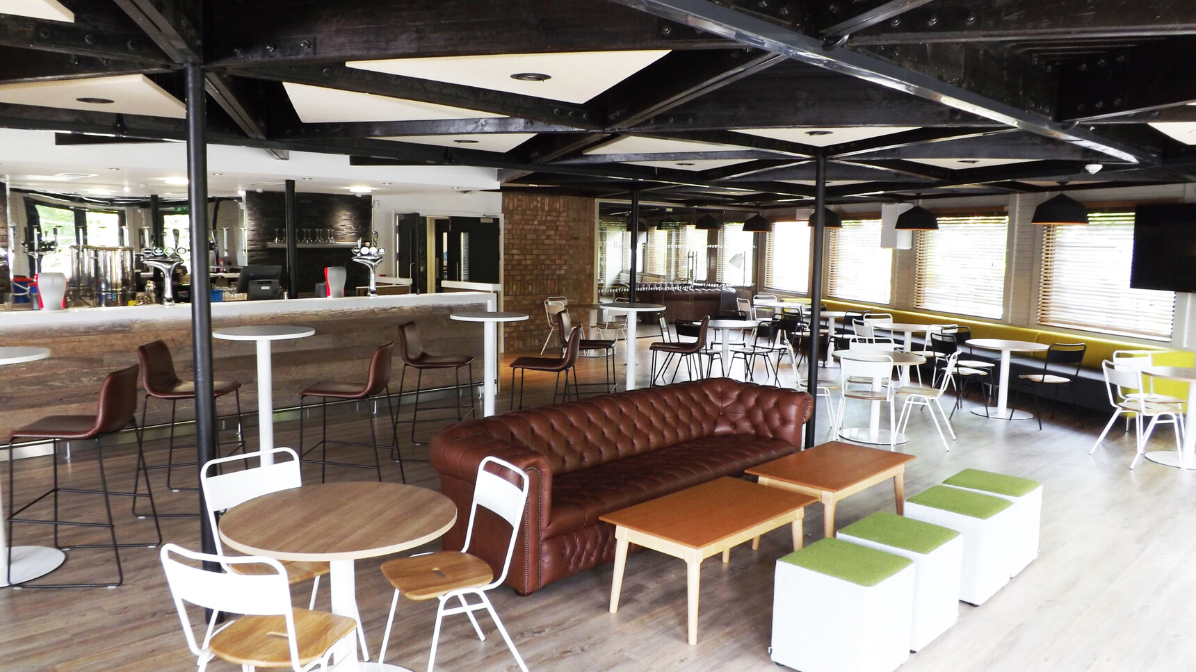 Four Elite Circular Bar Tables with Round 470mm Base With Grey Top And White Base Finish With Seven Circular Meeting Tables with Round 600mm Base With Wood Table Tops And White Bases In Canteen Bar Environment