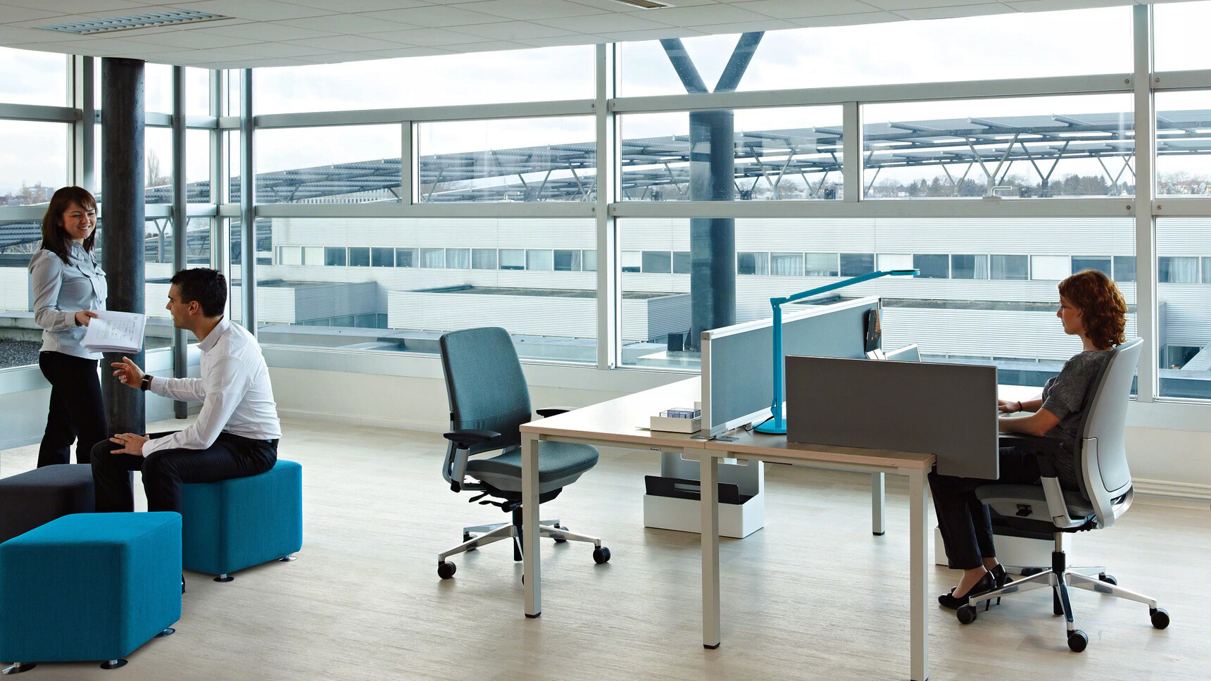 Two Steelcase Amia Platinum Office Task Chairs At Desks In Office Environment In Use By Three People