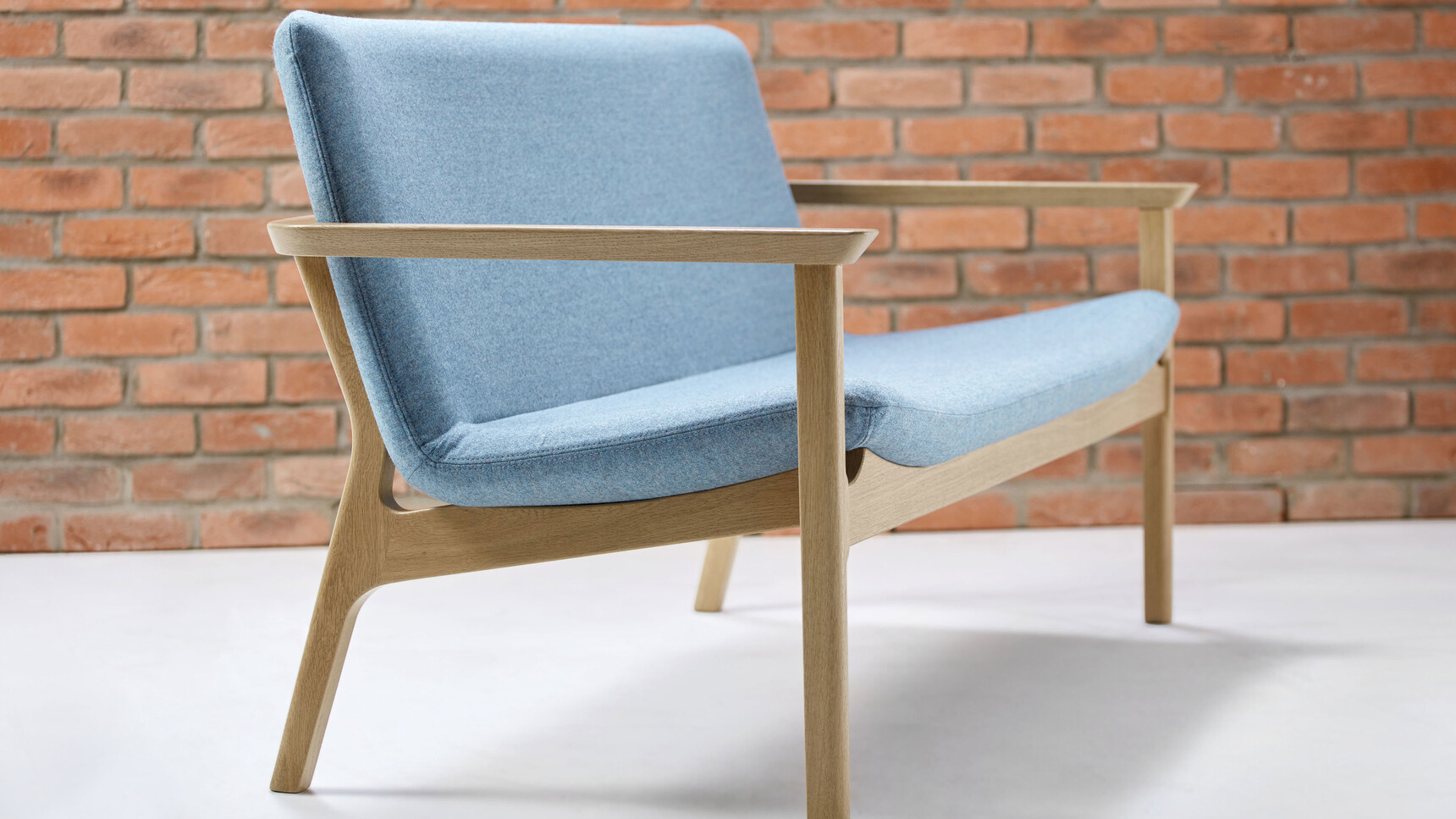 Connection Swoosh Two Seater Sofa With Arms In Blue Upholstery And Oak Frame And Base Detail Image With Brick Wall