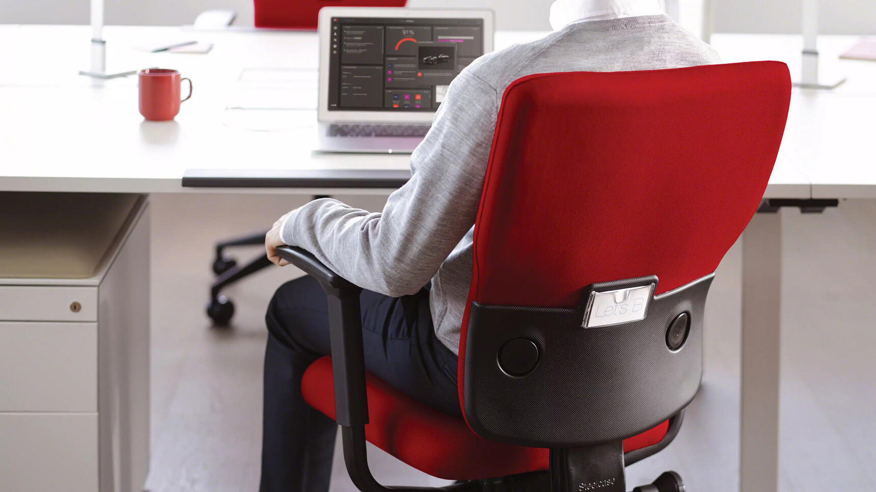 Steelcase Let's B High Back Office Chair Red Upholstery At Desk With Man On Chair In Office Environment