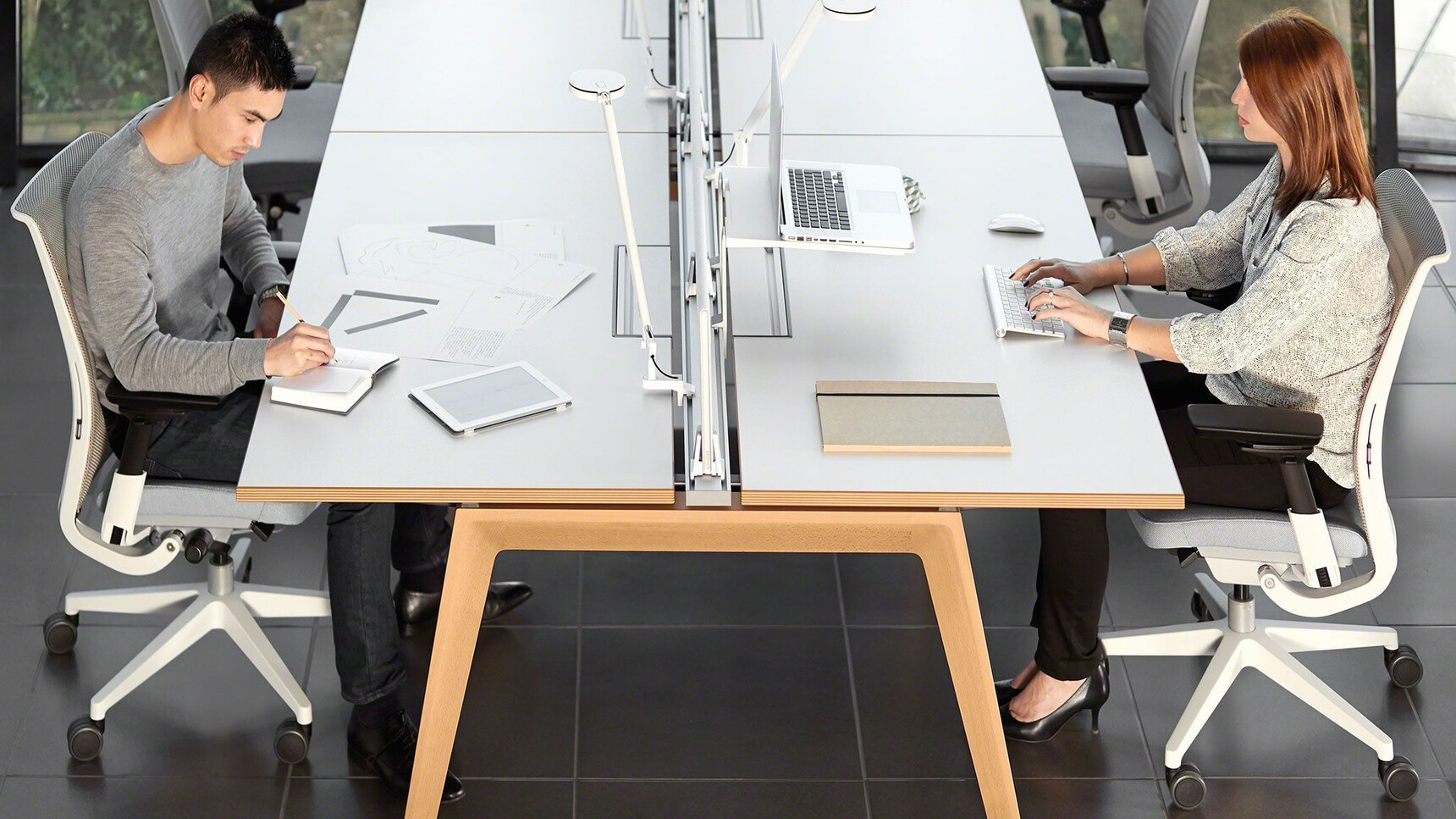 Steelcase Two B-Free Back to Back Desks With  White Table Top Finish With Wood Edges And Wood Leg Finish With Four Think Upholstered Office Chairs With Grey Upholstery And Light Grey Frame With Two People