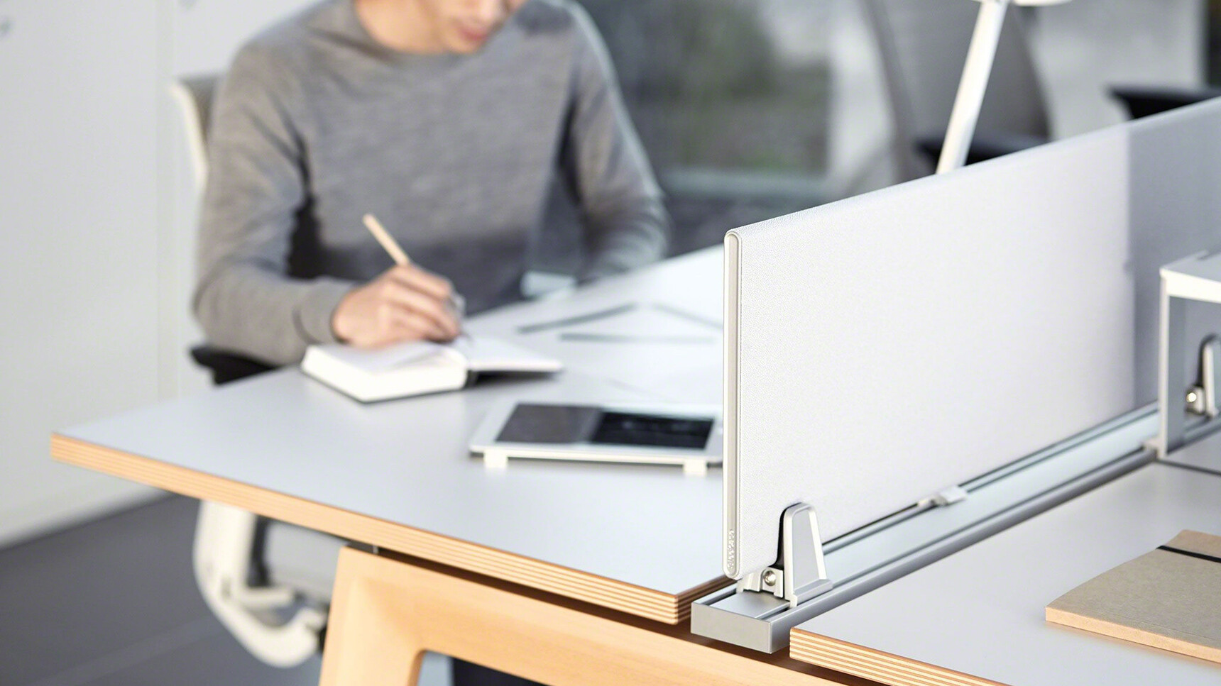 Steelcase Two B-Free Back to Back Desks With  White Table Top Finish With Wood Edges And Wood Leg Finish With Two Think Upholstered Office Chairs With Grey Upholstery And Light Grey Frame With Person At Desk