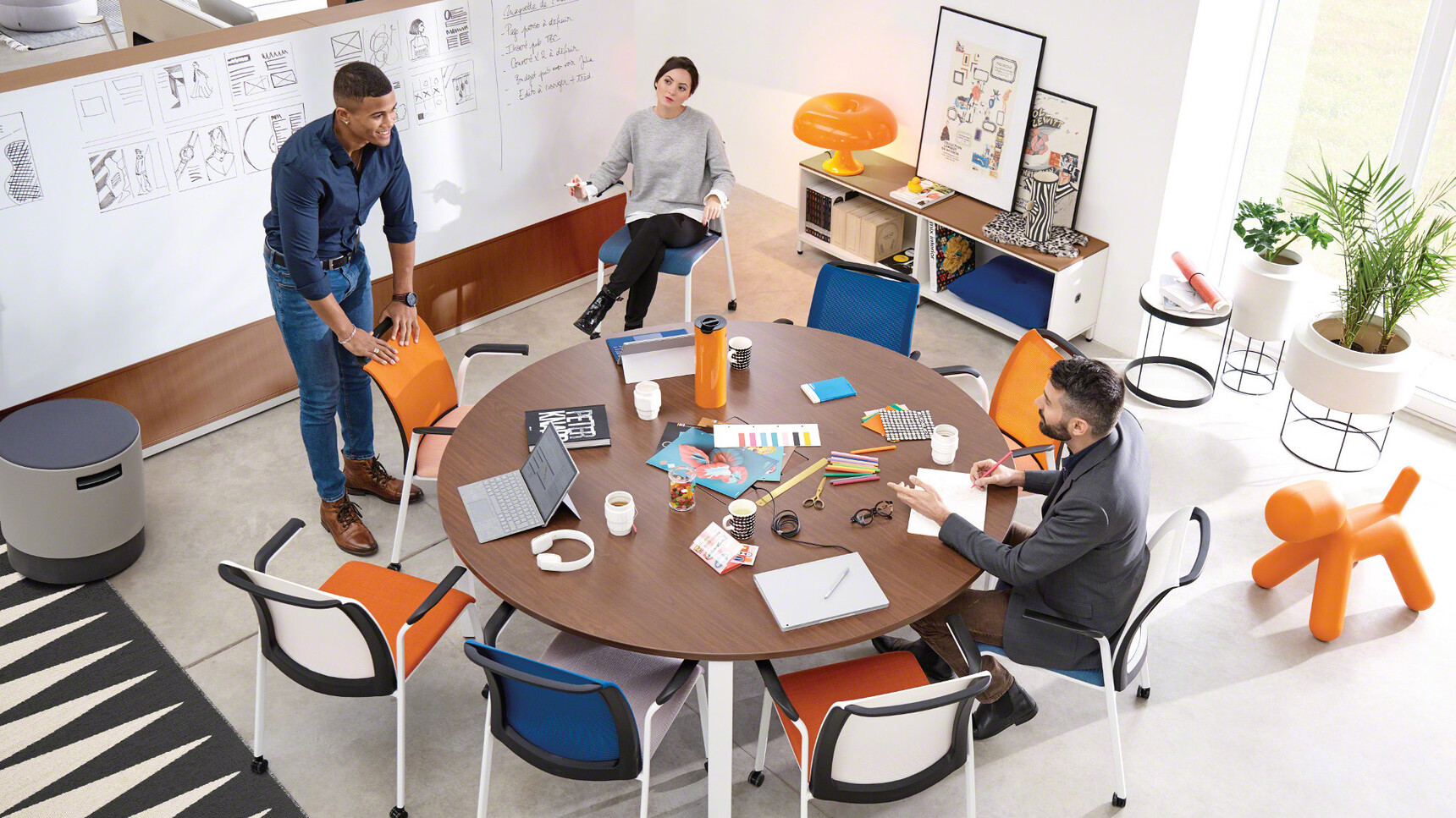 Eight Steelcase Eastside Four Leg Base Meeting Chairs In Orange And Blue Upholstery At Desk With Three People In Meeting Room Environment