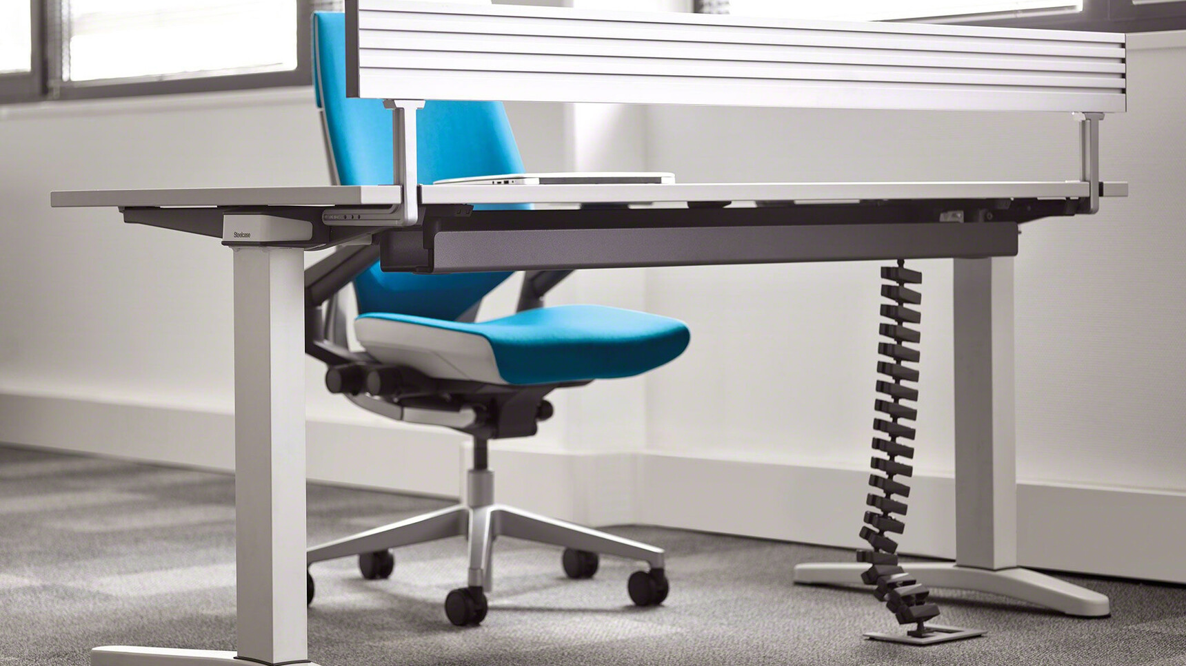 Steelcase Ology Fixed Height Desk With Metallic Table Top And Metallic Legs With Gesture Wrapped Back Office Chair With Light Blue Upholstery With Black Grey Frame And Polished Aluminium Base At Desk Detail Image