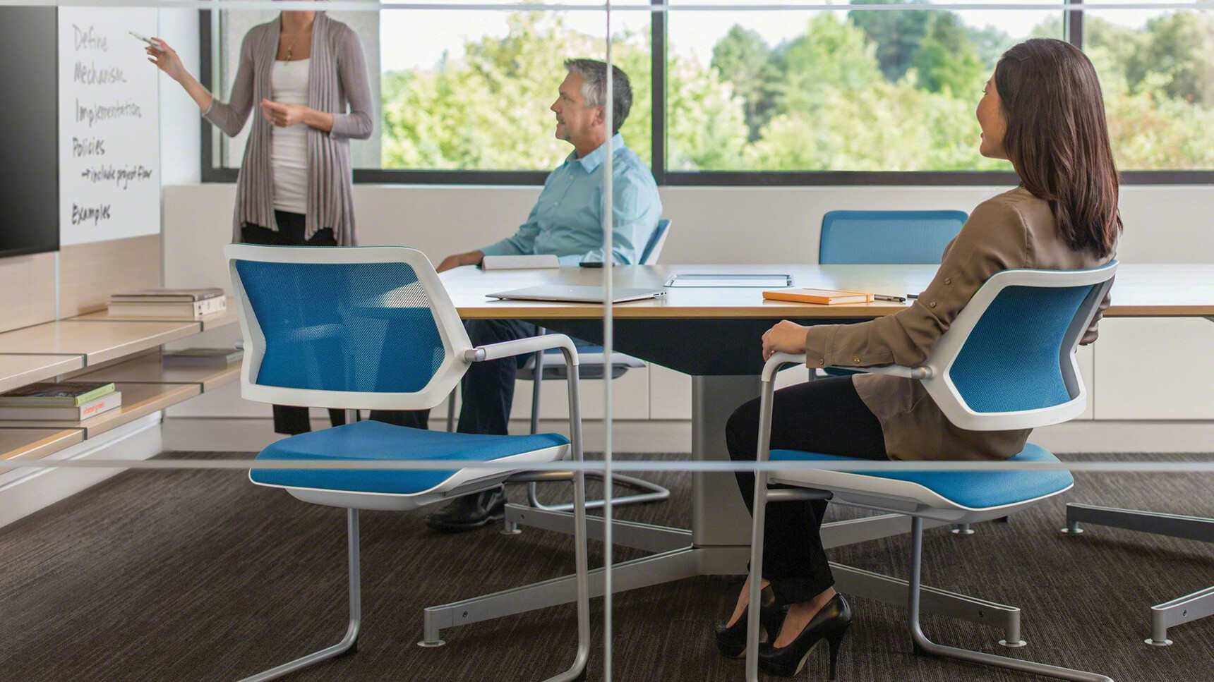 Four Steelcase Qivi Sled Base Conference Chairs With Blue Upholstery And White Frame And Platinum Base Finish At Steelcase Desk With Three People In Conference Room