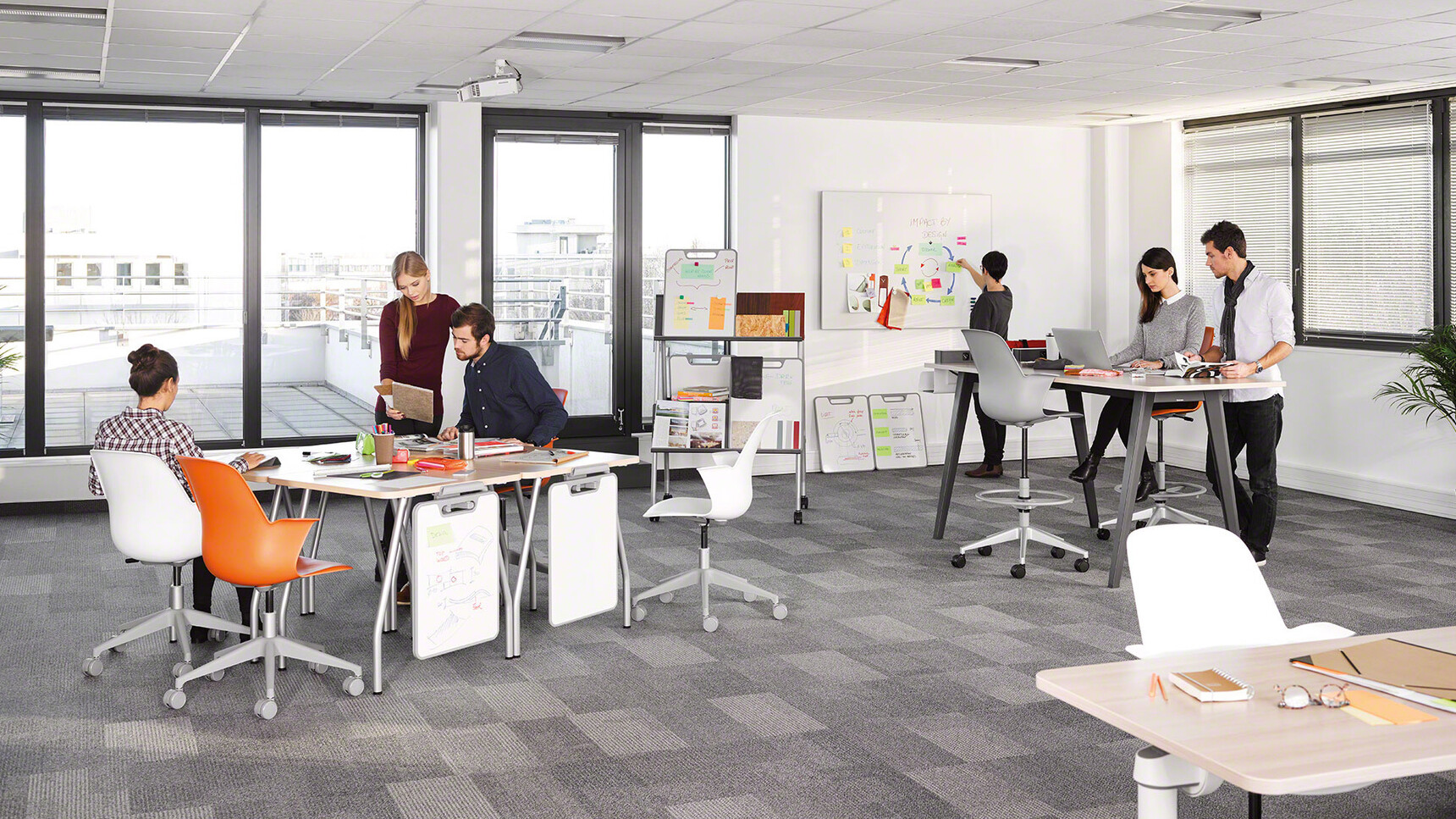 Two Steelcase Verb Rectangular Desks With Wood Table Top Finish And Grey Leg Finish With Optional White Board Easels With Four Node Chairs At Desk In Orange And White Upholstery In Use By Six People