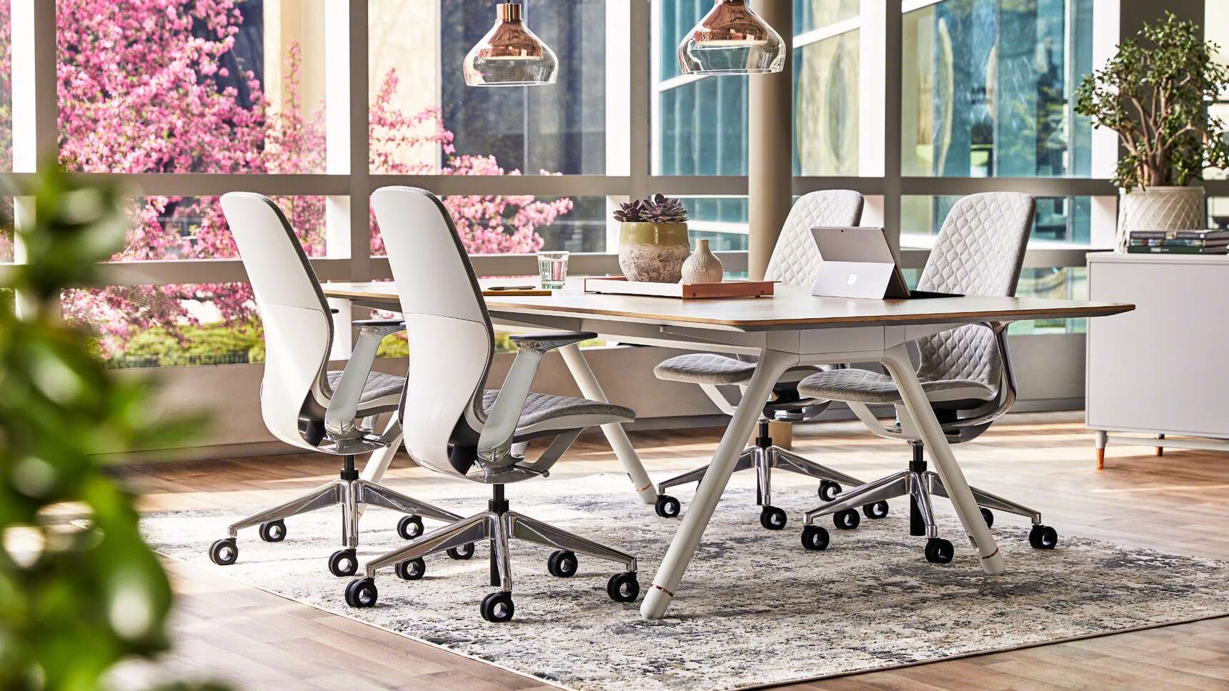 Four Steelcase SilQ Upholstered Office Chairs With Grey Upholstery With Chrome Legs On Castors And Chrome Fixed Arms And Matte Aluminium Frame At Fixed Height Desk In Office Setting