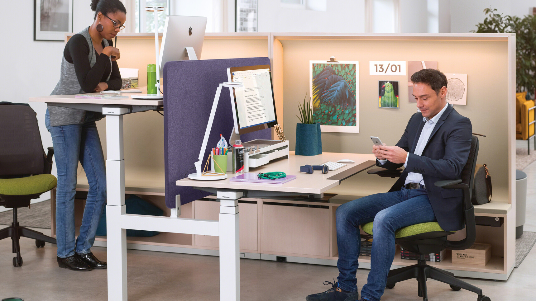 Steelcase Ology Height Adjustable Bench Desk with Simple Touch With Light Wood Table Top Finish And White Leg Finish And Purple Privacy Screen In Use By Two People