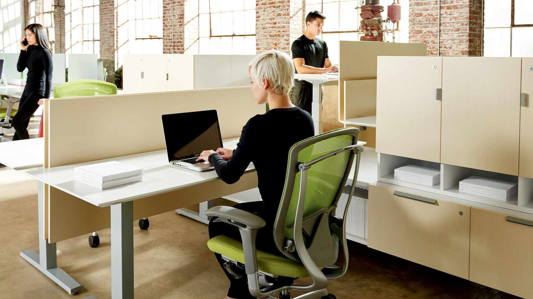 Three Okamura Contessa II Mesh Seat & Back Office Chairs With Green Cushion And Backrest With Grey Frame With Grey 4-D Adjustable Arms At Desks With Three People In Use One Using Chair