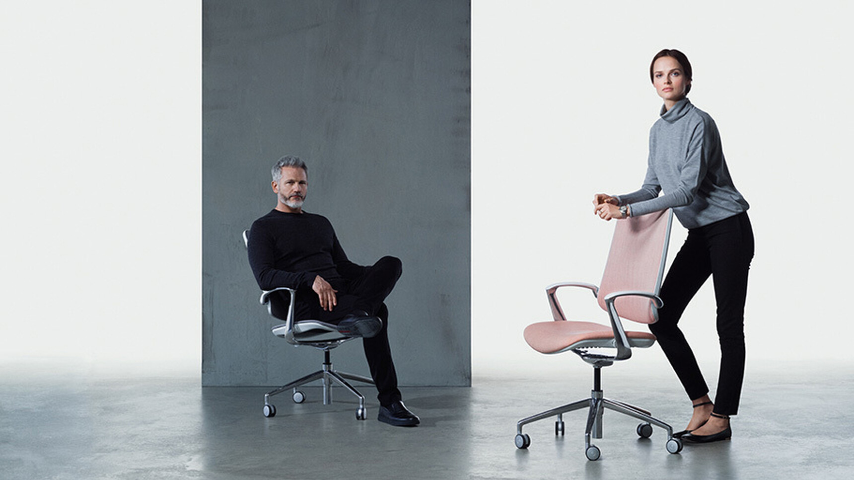 Two Boss Design Trinetic Upholstered Office Chairs One In Pink Upholstery And One In Dark Blue Upholstery Both With Polished Aluminium Armrests And Base On Castors In Use By A Man And Woman