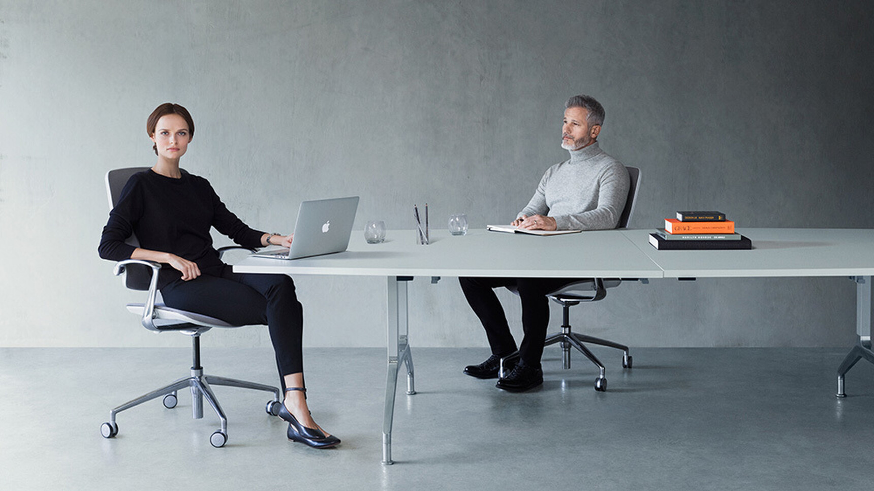 Two Boss Design Trinetic Upholstered Office Chairs With Light Grey Upholstery With White Frame Backrest And Polished Aluminium Armrests And Polished Aluminium Base On Castors At Desk In Use By Two People