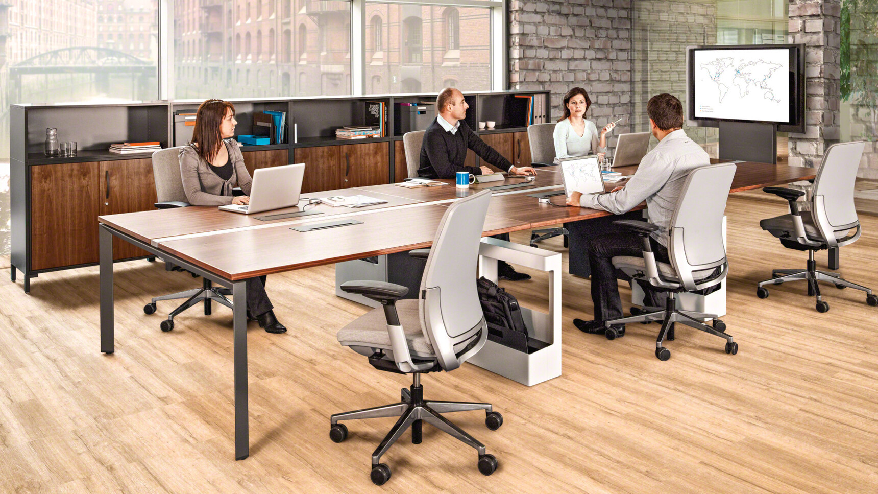Two Steelcase Frameone Bench Desks For Two With Black Free Standing Legs And Wood Table Top With Six Steelcase Office Chairs In Grey In Office Environment