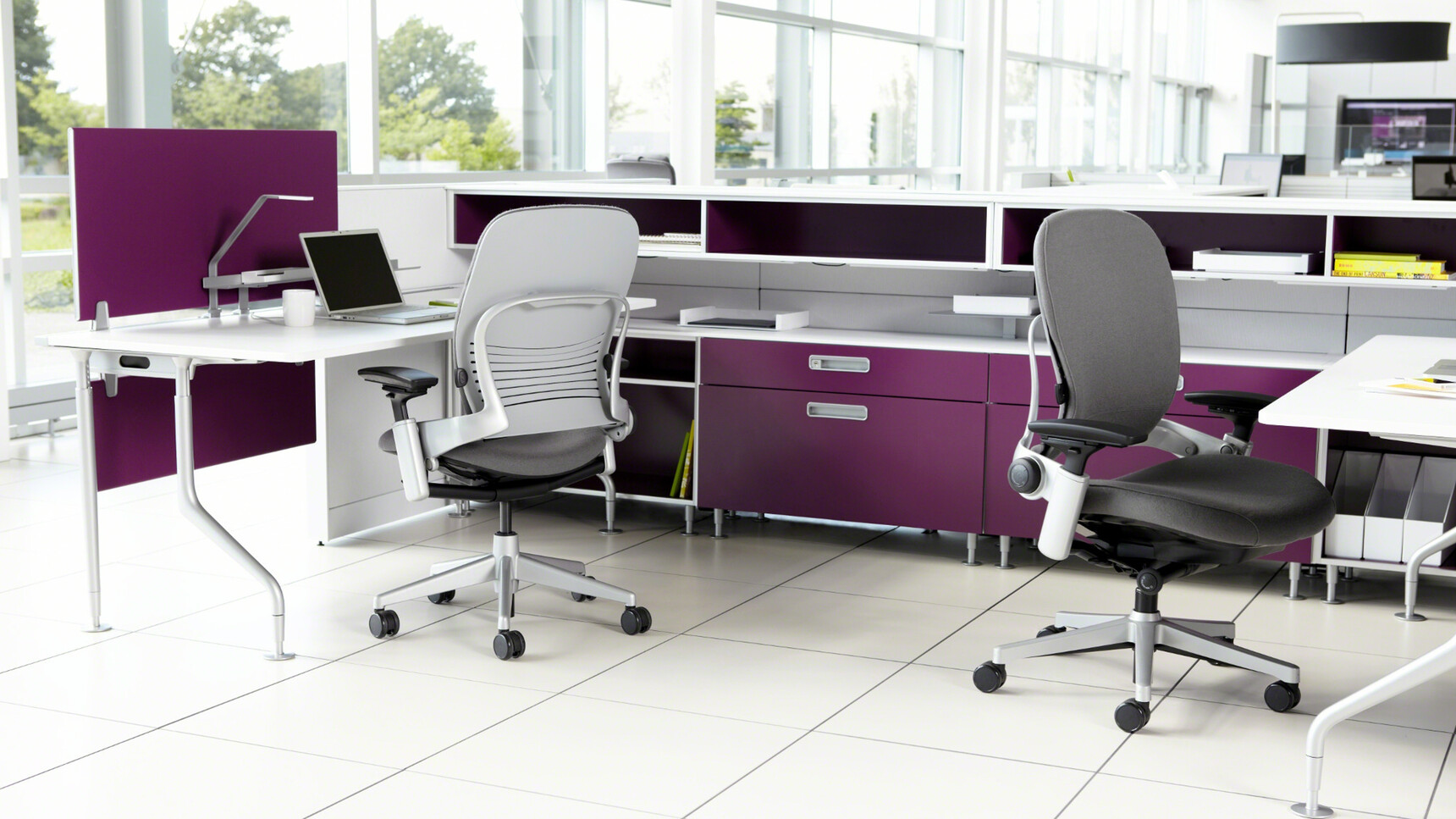 Two Steelcase Leap Upholstered Office Chairs With Grey Upholstery And 4-D Arm Options Showing One Front Angle View And One Back Angle View At Desk In Office Environment