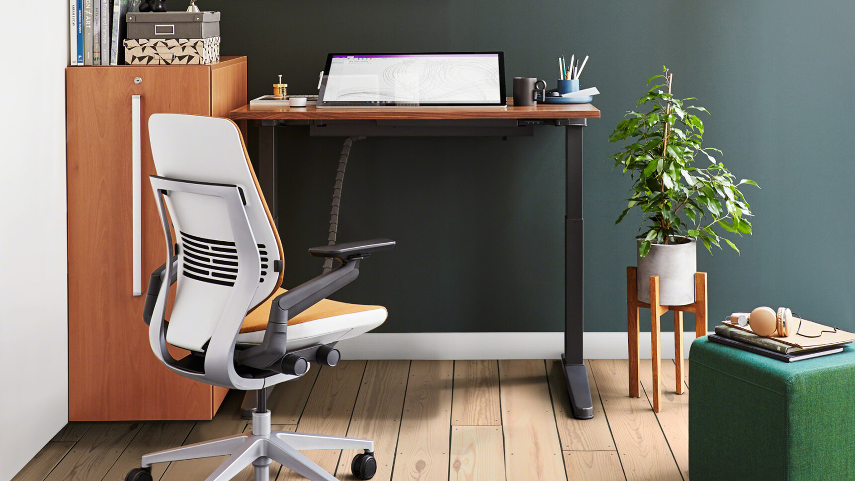 Steelcase Ology Height Adjustable Desks with Active Touch With Black Leg Finish And Wood Table Top Finish Extended To Middle Height Setting With Gesture Wrapped Back Office Chair With Orange Upholstery In Office Environment